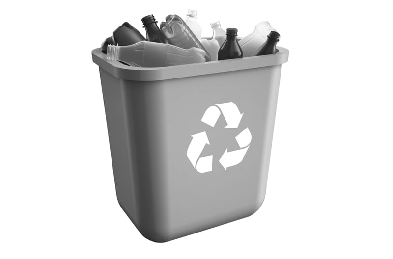 A bin with three arrows in a loop on the front denoting recycling, filled with empty plastic and glass bottles.