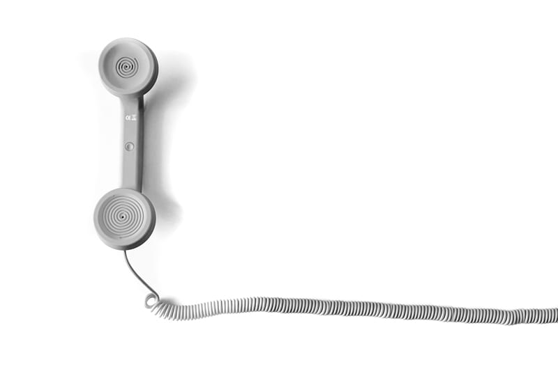 A telephone landline handset attatched to a curled cord.