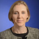 Claire Warnes looks into the camera in front of a bright blue background.