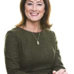 Fiona Cannon smiling, sits at a table with her hands clasped
