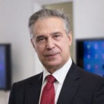 Frank Nigriello in dark suit and red patterned tie looks at the camera