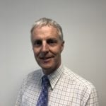 Ian Gibbs smiling in a checked shirt and blue tie