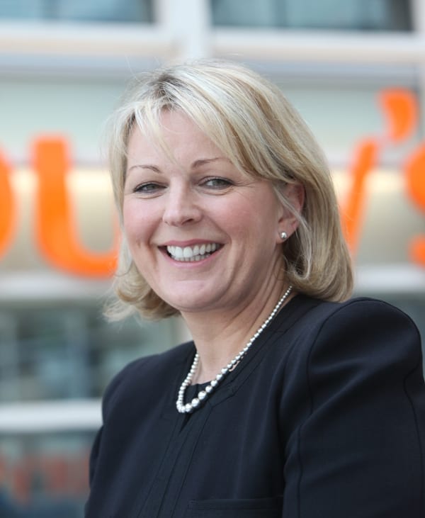 Judith Batchelar smiles in front of a large Sainsbury's logo