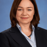 Lisa Donnelly in a navy suit and blue shirt, looks at the camera