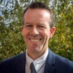 Simon Edwards stands in front of a hedge smiling