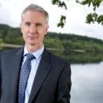 Richard Flint standing by a lake and wearing a suit