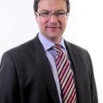 Richard Warneford in suit and striped tie looks at the camera