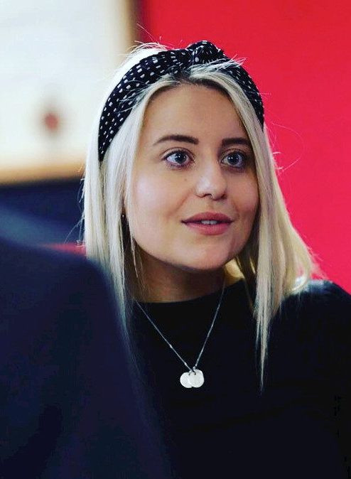 Aoife wearing a black headband and black top looks towards someone as they talk