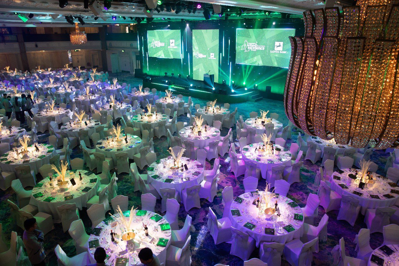 Tables set out a gala dinner infront of screens saying British Business Excellence Awards and Lloyds Bank. 