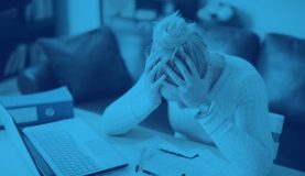 An image of a person sat at a desk with their head in their hands