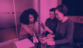 An image of 3 people smiling whilst looking at documents