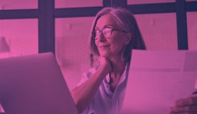 An image of a person working on a laptop and holding a piece of paper