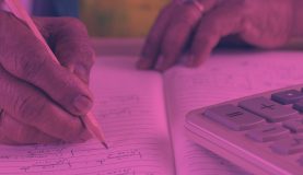 An image of a person writing on a piece of paper with a calculator to one side