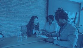 An image of 3 people sat round a desk smiling and looking at a document