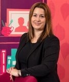 Annelie Grey smiling at the camera with a red background. 