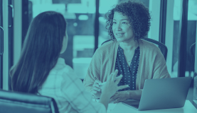 An image of two people in conversation with each other sat at a desk