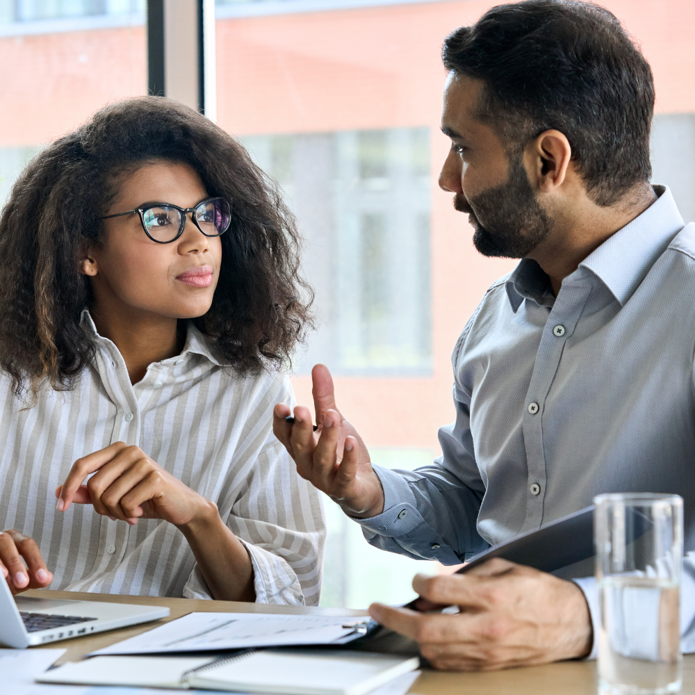 An image of two people sitting at a desk talking