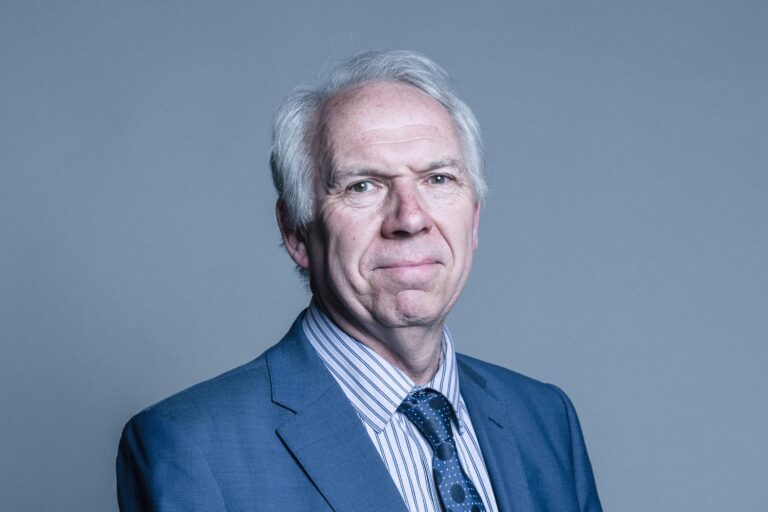 Lord Steve Bassam standing against a grey plain background.