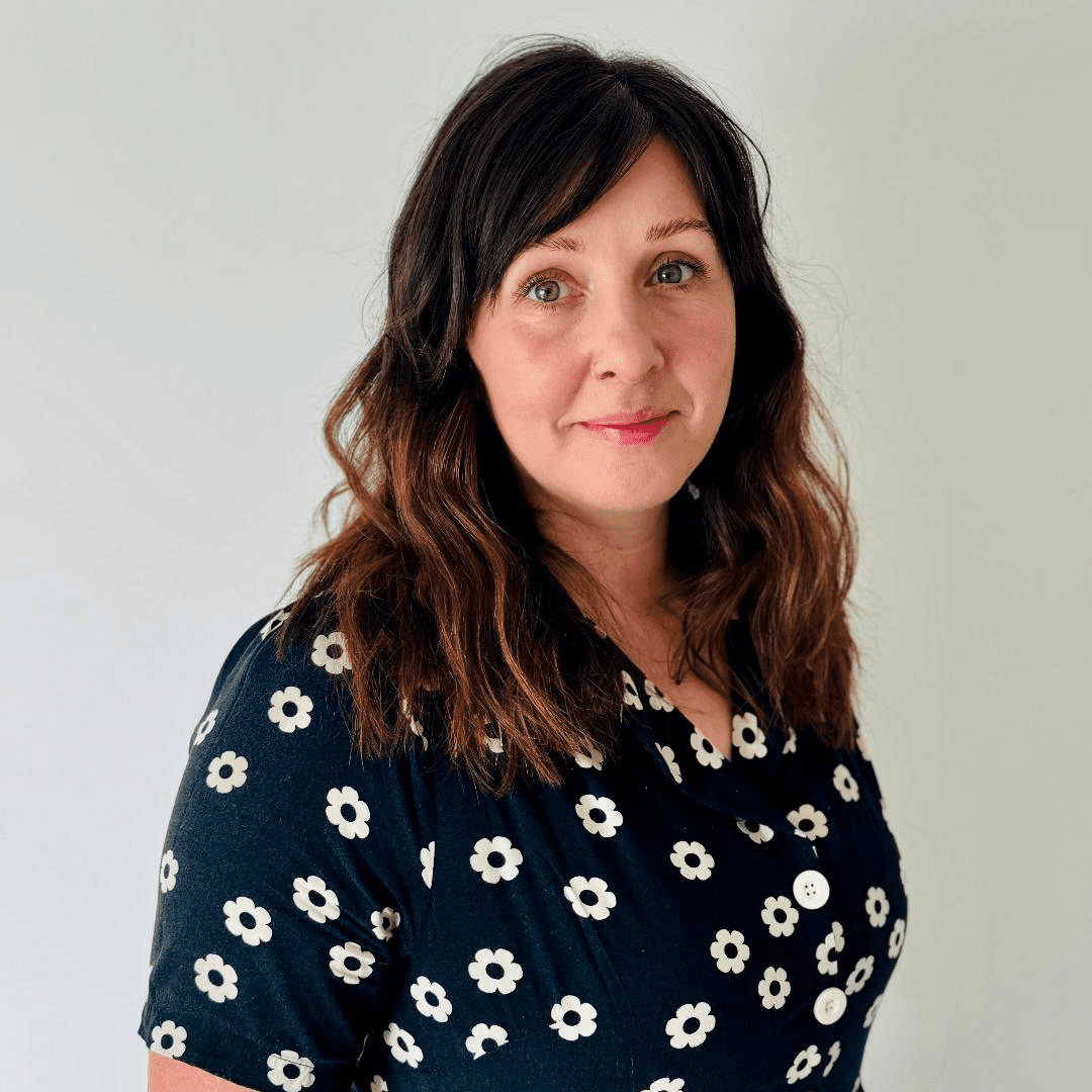 Simone Devinett looking at camera, standing against a white plain background.