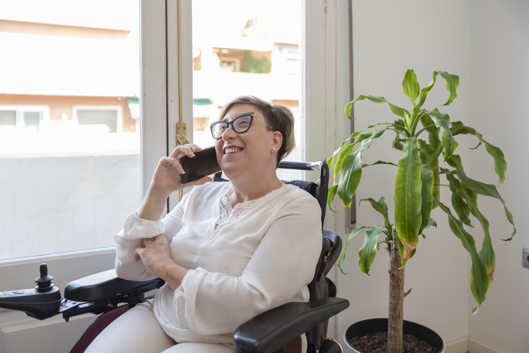 woman in wheelchair sitting next to window talking on phone